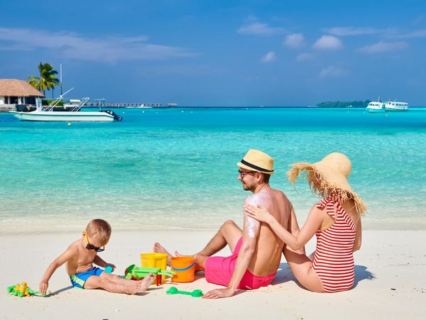 Family enjoying a sunny day at the beach with turquoise water and sand toys.