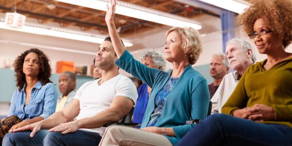 A woman raises her hand during a group meeting with diverse attendees.