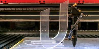 A 3D printer creating a transparent plastic object shaped like the letter U.