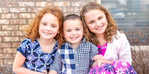 Three smiling children sitting closely together outdoors.