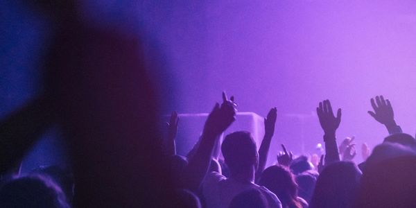 Crowd with raised hands enjoying a purple-lit concert or event.