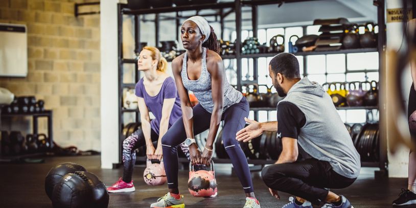 Women lifting kettlebells with trainer coaching.