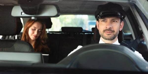 Taxi driver looking forward with female passenger in the backseat.