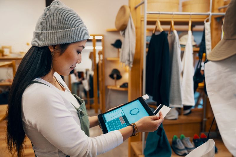 Retail shop clerk taking a mobile credit card payment on a digital tablet in a clothing boutique in Japan