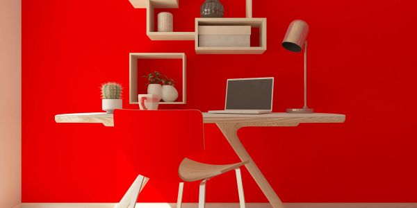 Modern wooden desk setup against a red wall.