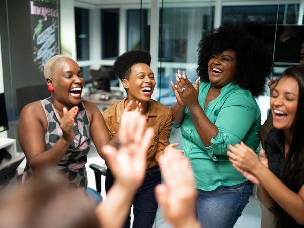 Group of women laughing and clapping indoors.