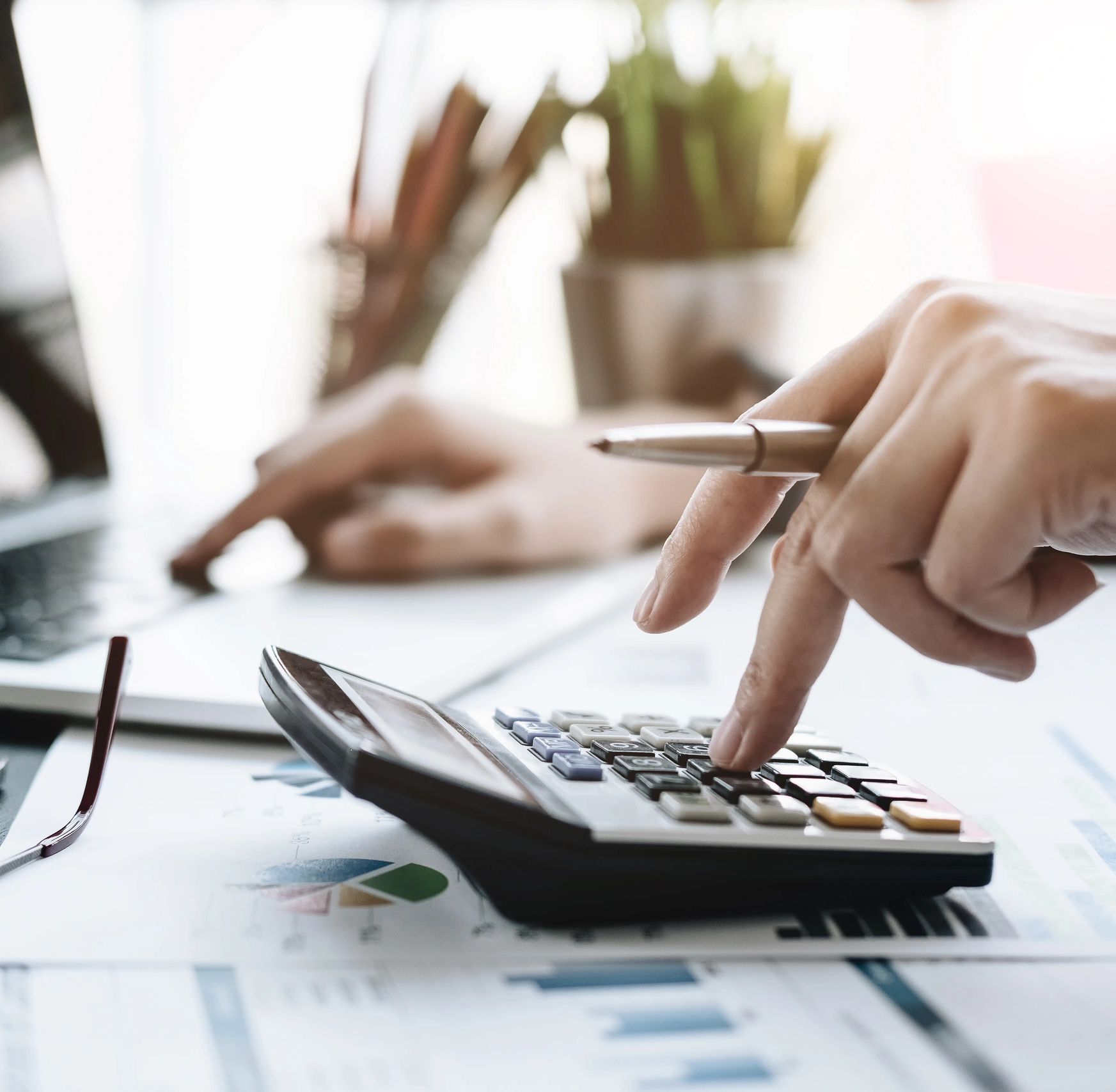 Person using calculator and laptop with financial documents on desk.