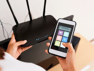 Person configuring a Wi-Fi router using a smartphone home network app.