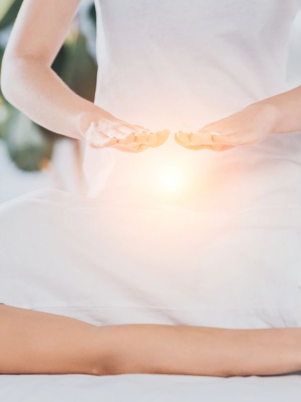Person receiving energy healing therapy with glowing hands above their abdomen.