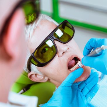 Dentist wearing blue gloves treating a patient with protective glasses in a dental clinic.
