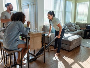Woman vacuuming floor while two people watch in the living room.