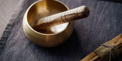 A brass singing bowl with a wooden striker on a dark fabric.