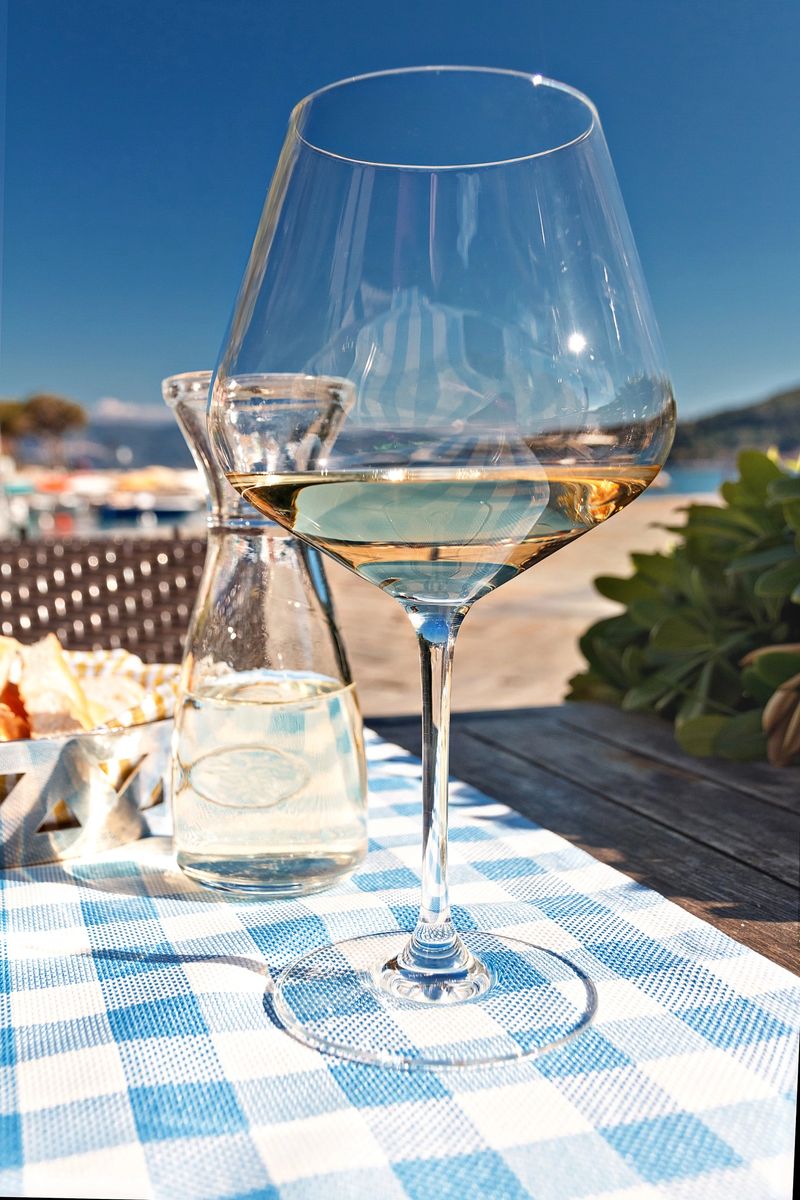 Transparent glass of white wine with water on a white and blue tablecloth on the Mediterranean coast in Italy on hot sunny day