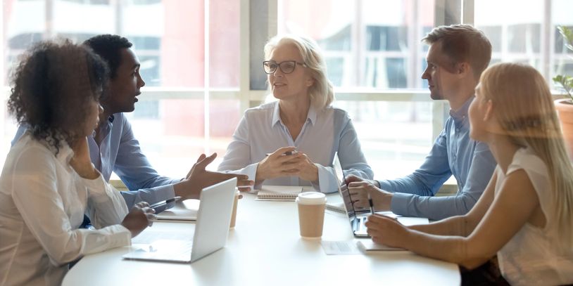 A diverse team engaged in a focused business meeting around a white table. HR Services. Client Testimonials. HRInsight.org