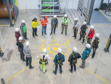 Group of people in safety gear gathered in a circle indoors.