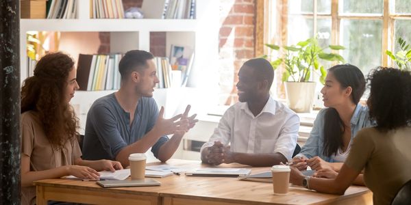 Five diverse coworkers engage in a lively meeting around a wooden table.