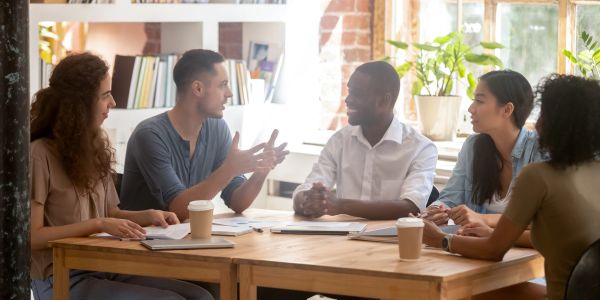 Five diverse coworkers engage in a lively meeting around a wooden table.