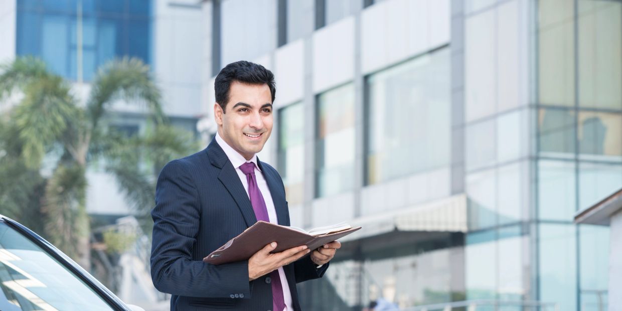 Confident businessman in a suit holding a folder outside a modern office building.