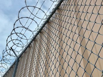 Chain-link fence topped with coiled razor wire against a cloudy sky.