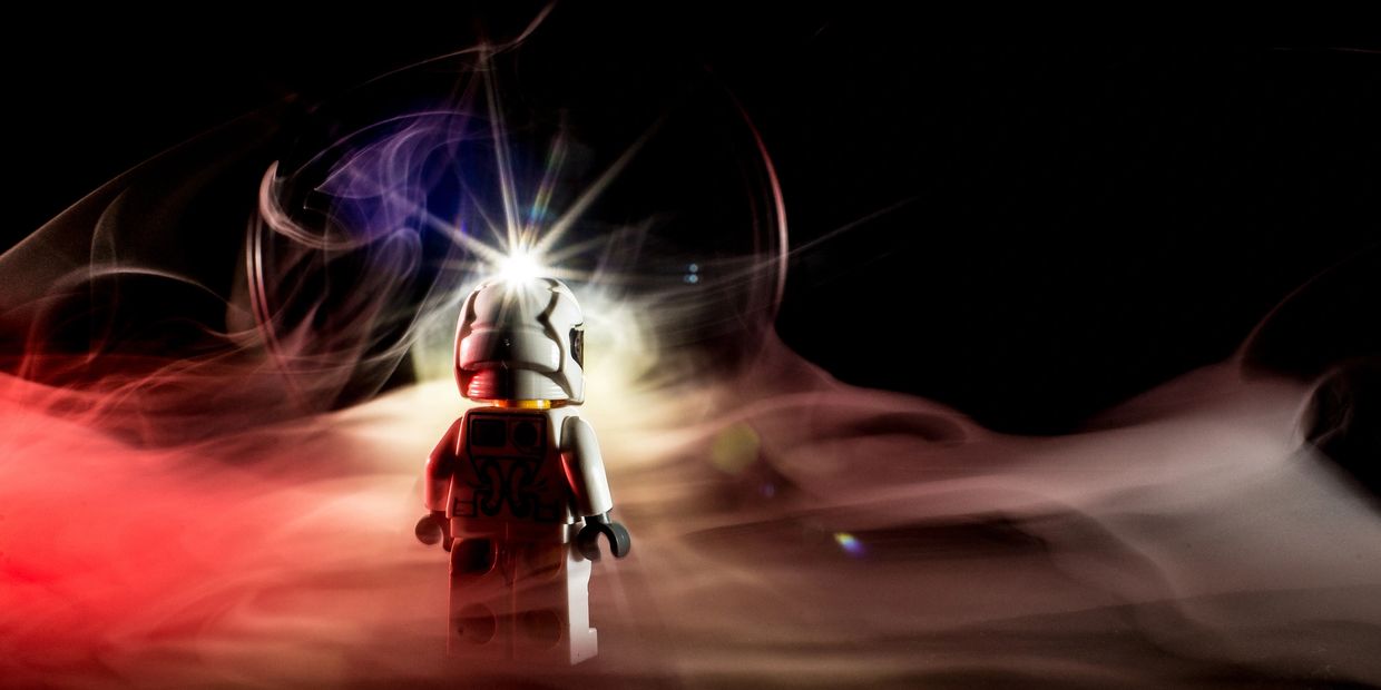 A LEGO astronaut figure surrounded by colorful smoke and bright light effects.