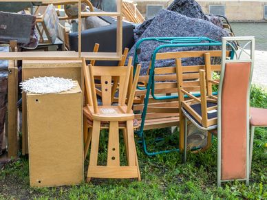 A pile of discarded wooden chairs and furniture outdoors on grass.
