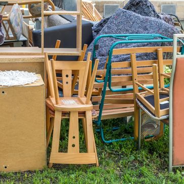 A pile of discarded wooden chairs and furniture outdoors on grass.