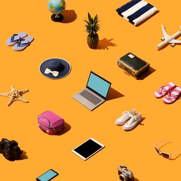 Travel essentials including laptop, suitcase, shoes, and camera arranged on orange background.