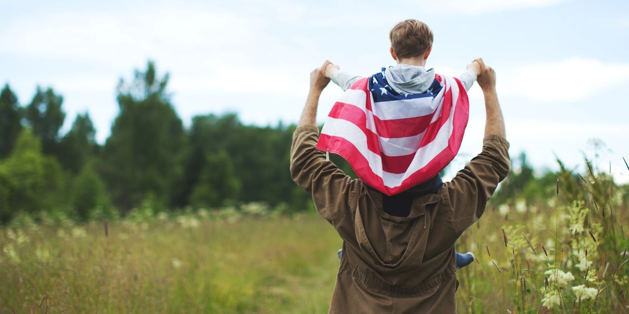 Child with American flag on shoulders riding on adult's shoulders.