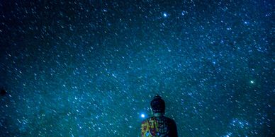 A statue gazing at a star-filled night sky with a blue hue.