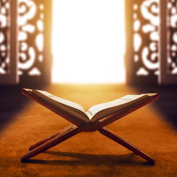 Open holy book on wooden stand illuminated by warm sunlight through ornate doors.