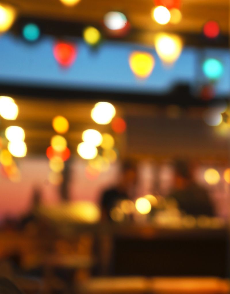Blurred background of people sitting at restaurant, bar or night club with colorful lights bokeh. Abstract defocused blur background.