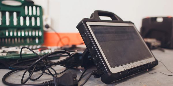A rugged tablet with cables on a workbench.