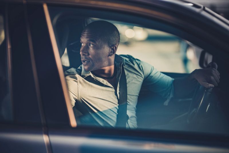 Mid adult African American businessman going on a trip by car while driving it in a reverse.