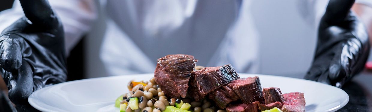 Chef presenting a gourmet plate with sliced steak and beans.