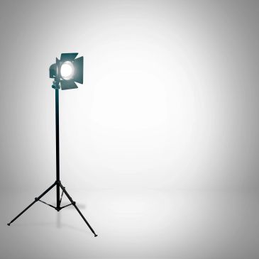 A studio spotlight on a tripod stand shining brightly against a plain background.