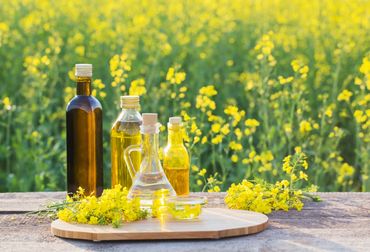 Bottles of cooking oil with yellow flowers on a wooden table in a field.