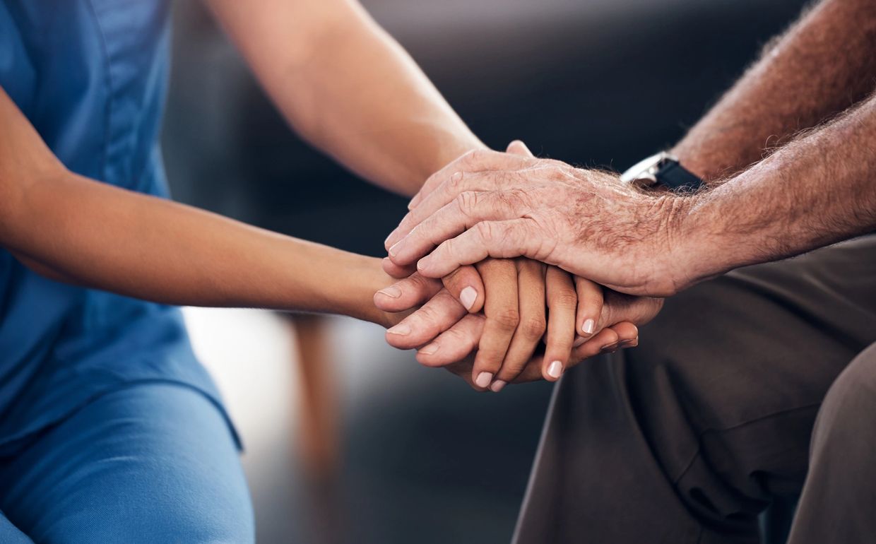A nurse gently holding an elderly patient's hands in a comforting gesture.