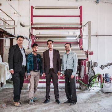 Four men standing in front of industrial machinery in a factory setting.