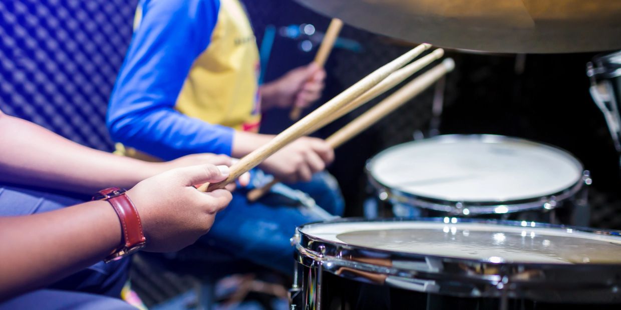 Close-up of hands playing drums with sticks in a music practice room.
