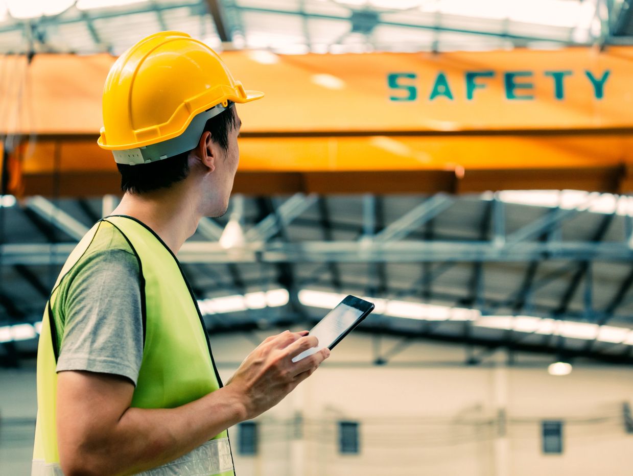 Worker in yellow helmet using a tablet at a safety zone.