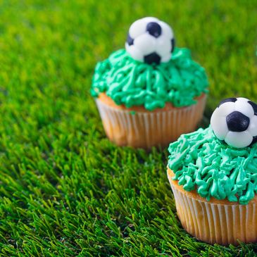 Cupcakes decorated with green frosting and soccer ball toppers on grass.