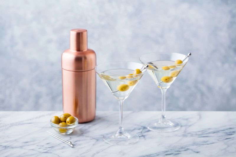 Martini cocktail with green olives, shaker on marble table background