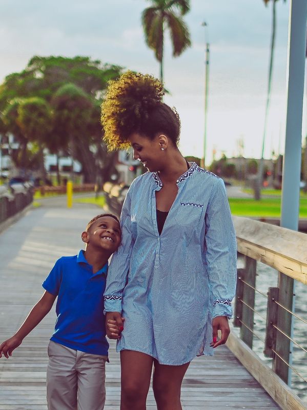 A woman and a boy holding hands and smiling on a boardwalk.