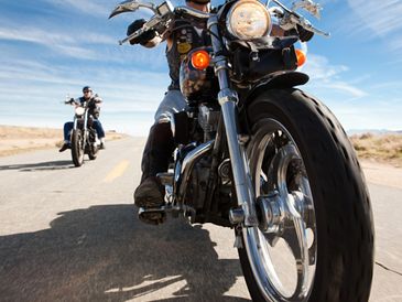 Two bikers riding motorcycles on an open road under a clear blue sky.