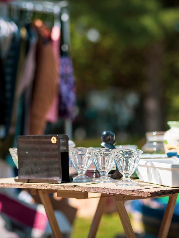 Outdoor flea market table with glassware and clothes rack in background.