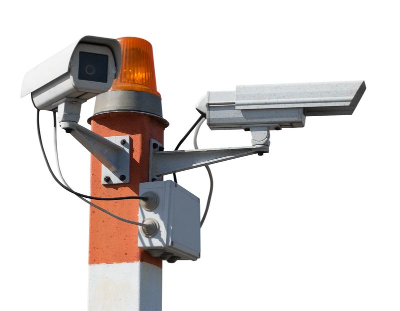 Two CCTV security cameras on red striped pillar with orange flashing light. Isolated on a white background