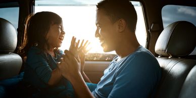 Father and daughter joyfully playing together in a car at sunset.