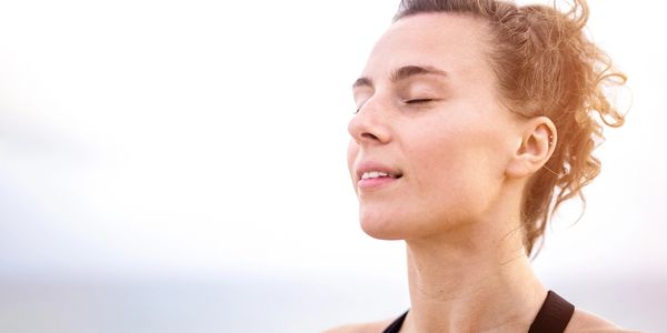 Woman peacefully meditating outdoors with eyes closed and sunlight on her face.