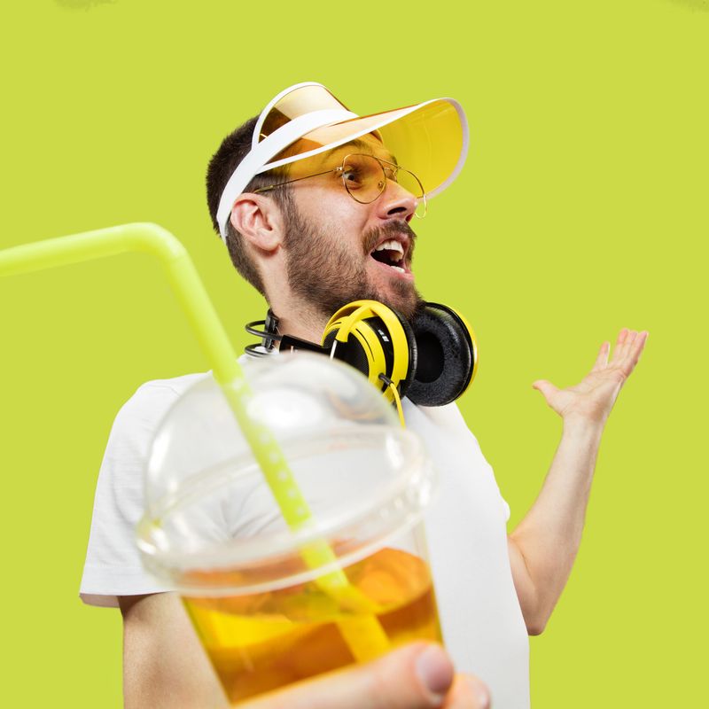 Happy meeting. Half-length close up portrait of young man in shirt on yellow background. Male model with headphones and drink. The human emotions, facial expression, summer, weekend concept.