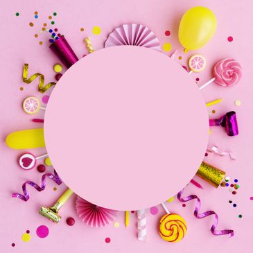 Colorful party decorations and candies arranged in a circle on pink background.